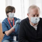 Medical nurse doing checkup to senior man patient during coronavirus outbreak home visit