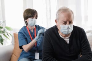 Medical nurse doing checkup to senior man patient during coronavirus outbreak home visit