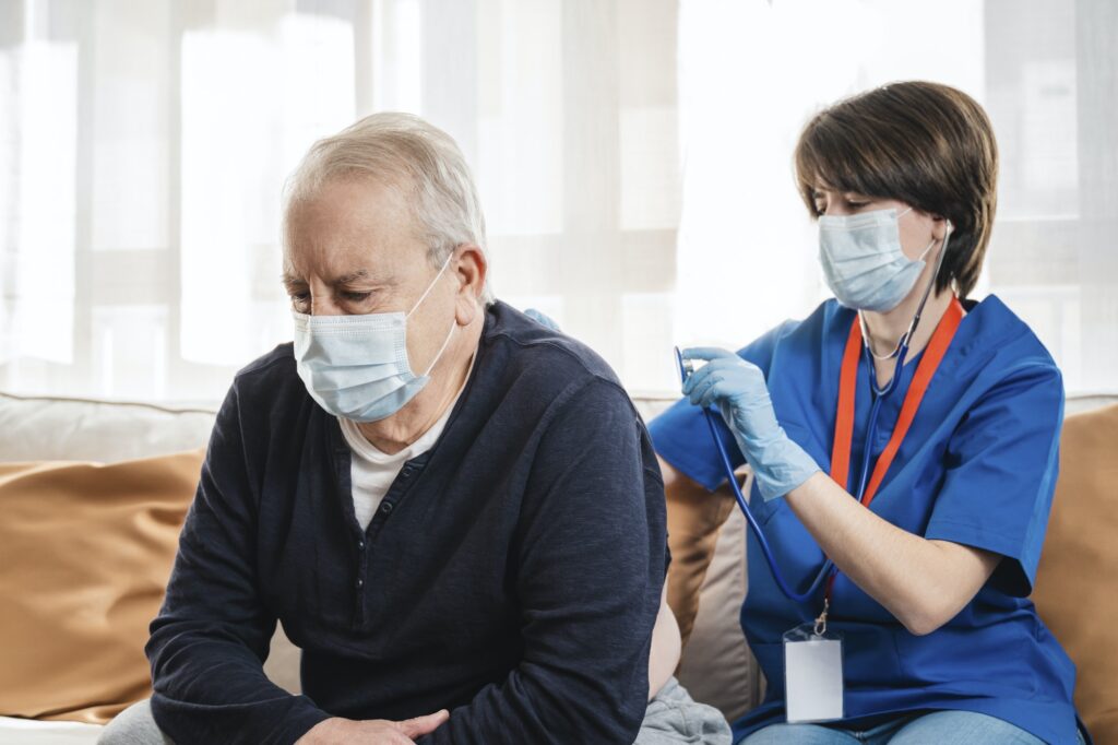 Medical nurse doing checkup to senior man patient during coronavirus outbreak home visit